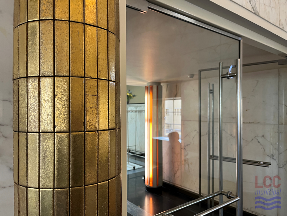 A close up picture of one of the gold-tiled columns which line the Assembly Hall. This one is seen at the entrance, next to a clear glass door with a steel metal frame.