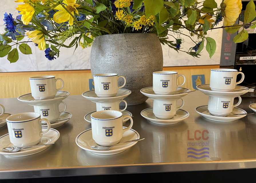 A set of cups with the Hilversum coat of arms on each. They are arranged on a table with a floral display behind.