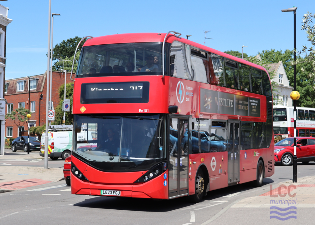 The bus is a fairly new red double decker with rather rounded features, giving it a steam-lined appearance. It is seen on an urban street with shops and flats in the background. It is going over a zebra crossing.
