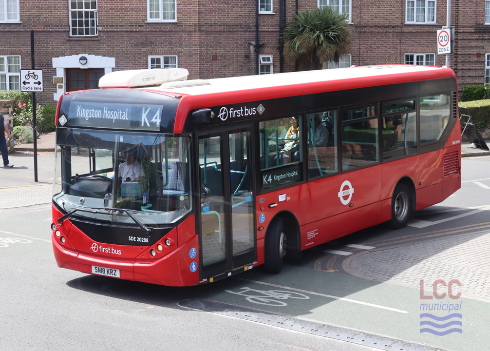 The bus is a red single decker. It is on the K4 to Kingston Hospital. In the background is a large brick-built mansion block of flats.