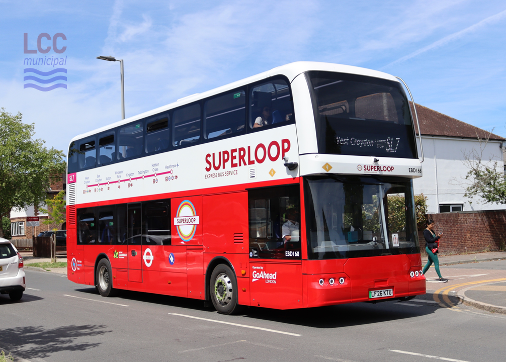 The bus is in Superloop branding, which sees the bottom half of the bus painted red and the upper part painted white. The route taken is clearly indicated along the side of the bus. The side also includes a large Superloop logo, which is a variant of the London Transport roundel. The bus is shown on a suburban street.