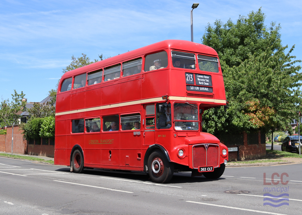 RM1363, a red double deck front-engine rear-entrance bus. It is travelling toward the camera on a suburban street with houses and trees behind. It carries no advertising.