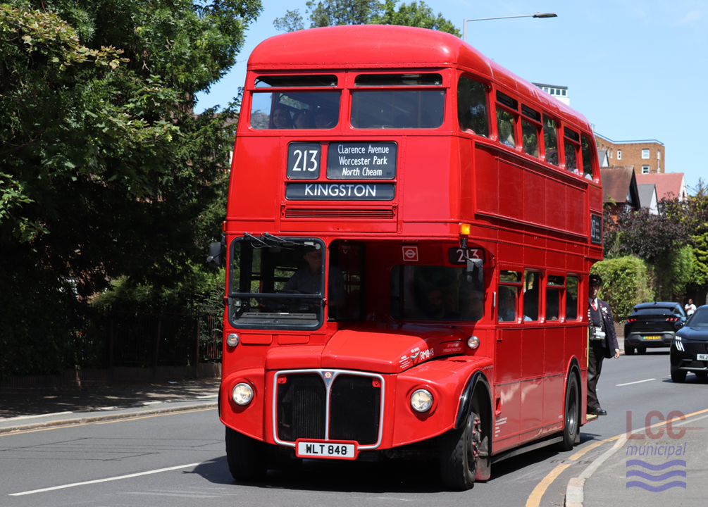 RM848, a red double deck front-engine rear-entrance bus. It is travelling toward the camera on Kingston Hill with houses, a block of flats and trees behind. It carried no advertising.