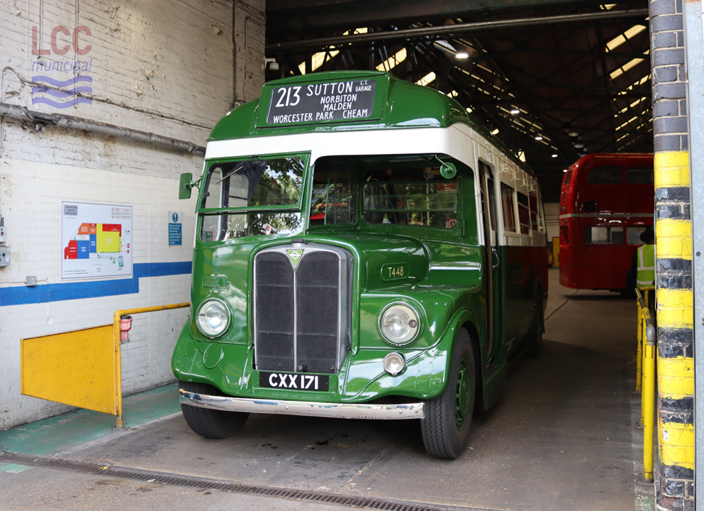 AEC Regal T448 is a single deck, green coach with a white band surrounding the saloon windows. It is shown parked in an entrance to Sutton Garage, the factory-like gloom of which can be seen behind.